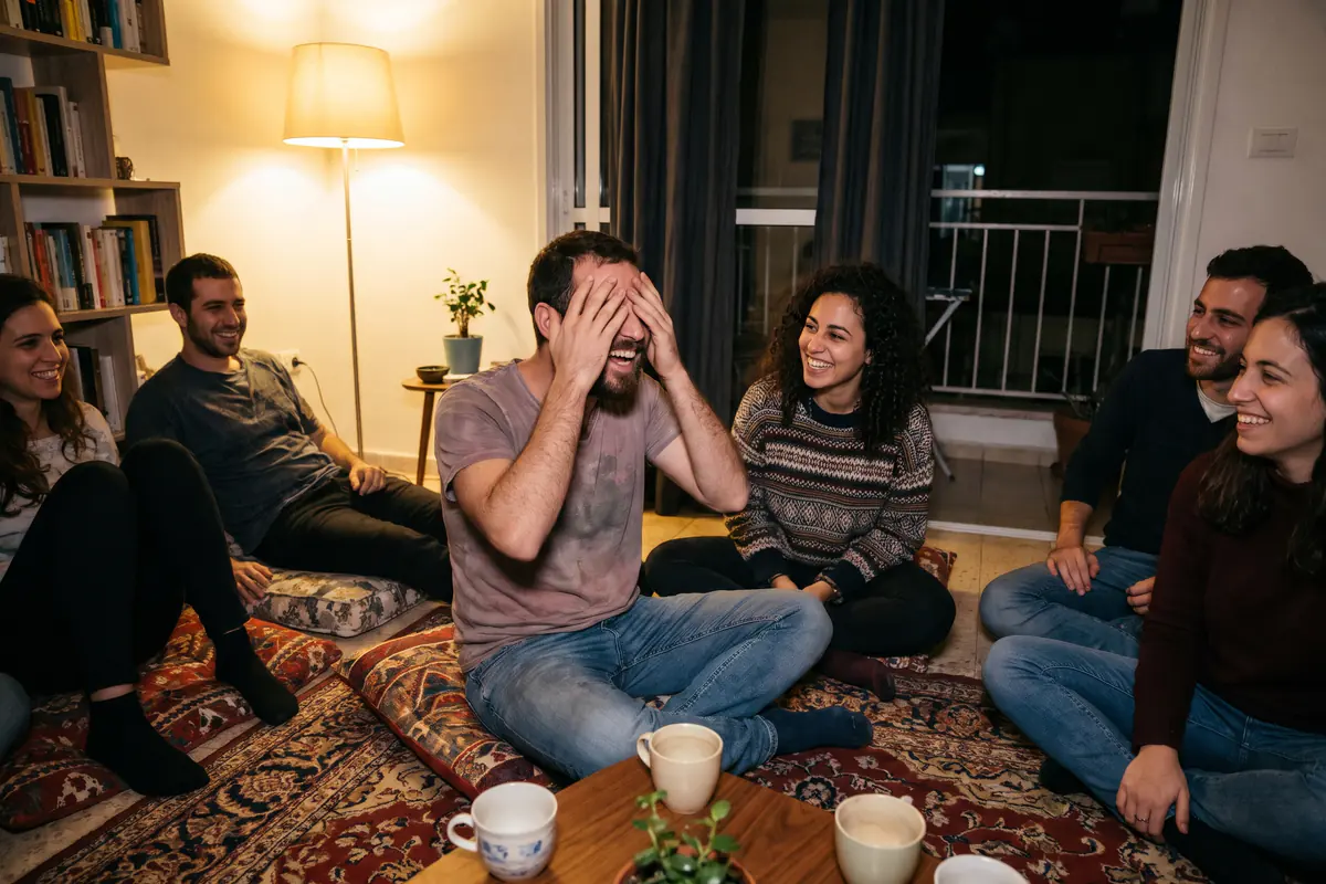 חבורה יושבת על כריות בסלון בלילה וצוחקת משאלות שוברות קרח