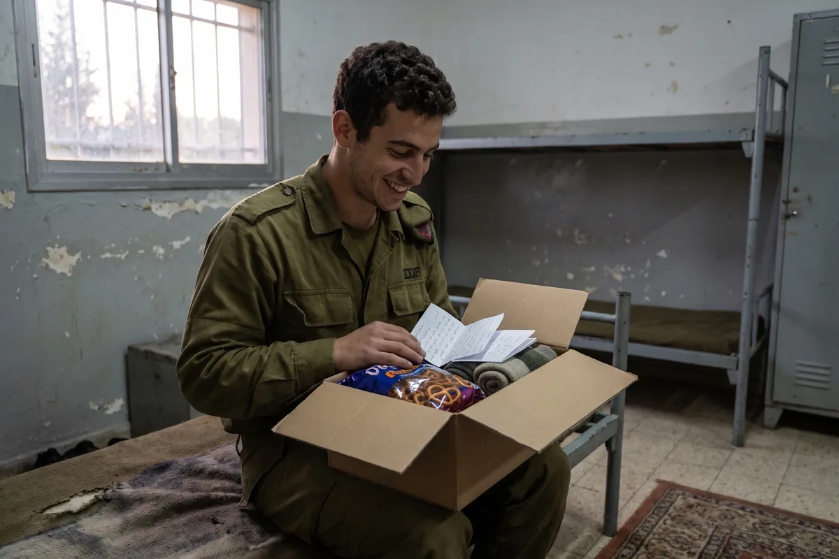 חייל במילואים פותח חבילה מהבית: מתנה לבן הזוג עם חטיפים ופתקים, על מיטה בבסיס
